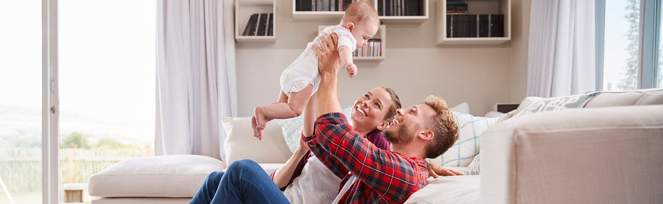 A young, happy couple playing with their baby in a spacious living room.