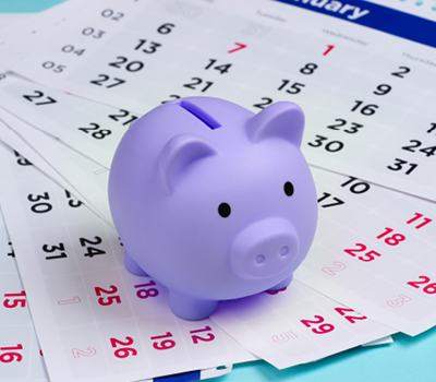 A light blue piggy bank on a pile of calendar sheets.