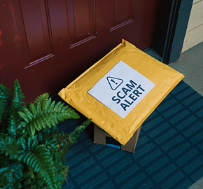 A package at a doorstep with a sign on it saying "Scam Alert".